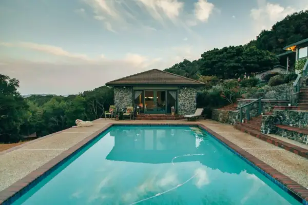Piscina con agua cristalina, rodeada de vegetación y una casa de piedra. Ideal para climatizar piscina y disfrutar todo el año.