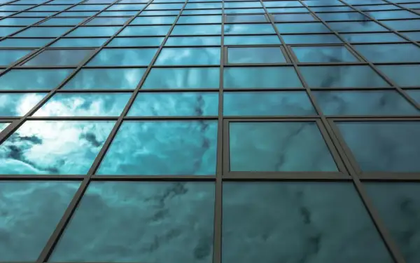 Fachada de edificio con cristales fotovoltaicos reflejando un cielo nublado y azul.