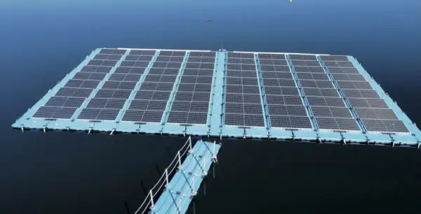 Plataforma de energía fotovoltaica flotante sobre un cuerpo de agua azul, con un pasarela azul conectada.