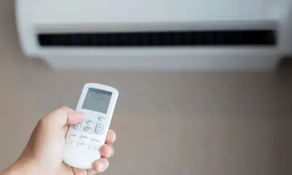 Mano sujetando control remoto de aire acondicionado para combatir el calor. La pantalla muestra 25 grados.