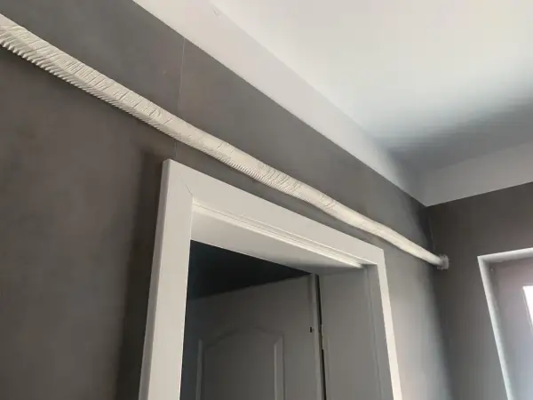 Ideas para tapar tubos aire acondicionado: un tubo blanco texturizado recorre la pared gris sobre un marco de puerta blanco.