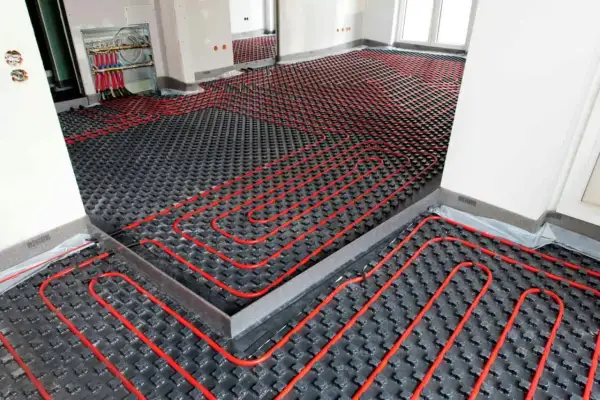 Instalación de sistema de calefacción por suelo radiante, con tuberías rojas sobre paneles negros. La temperatura del suelo radiante se controla desde un colector.